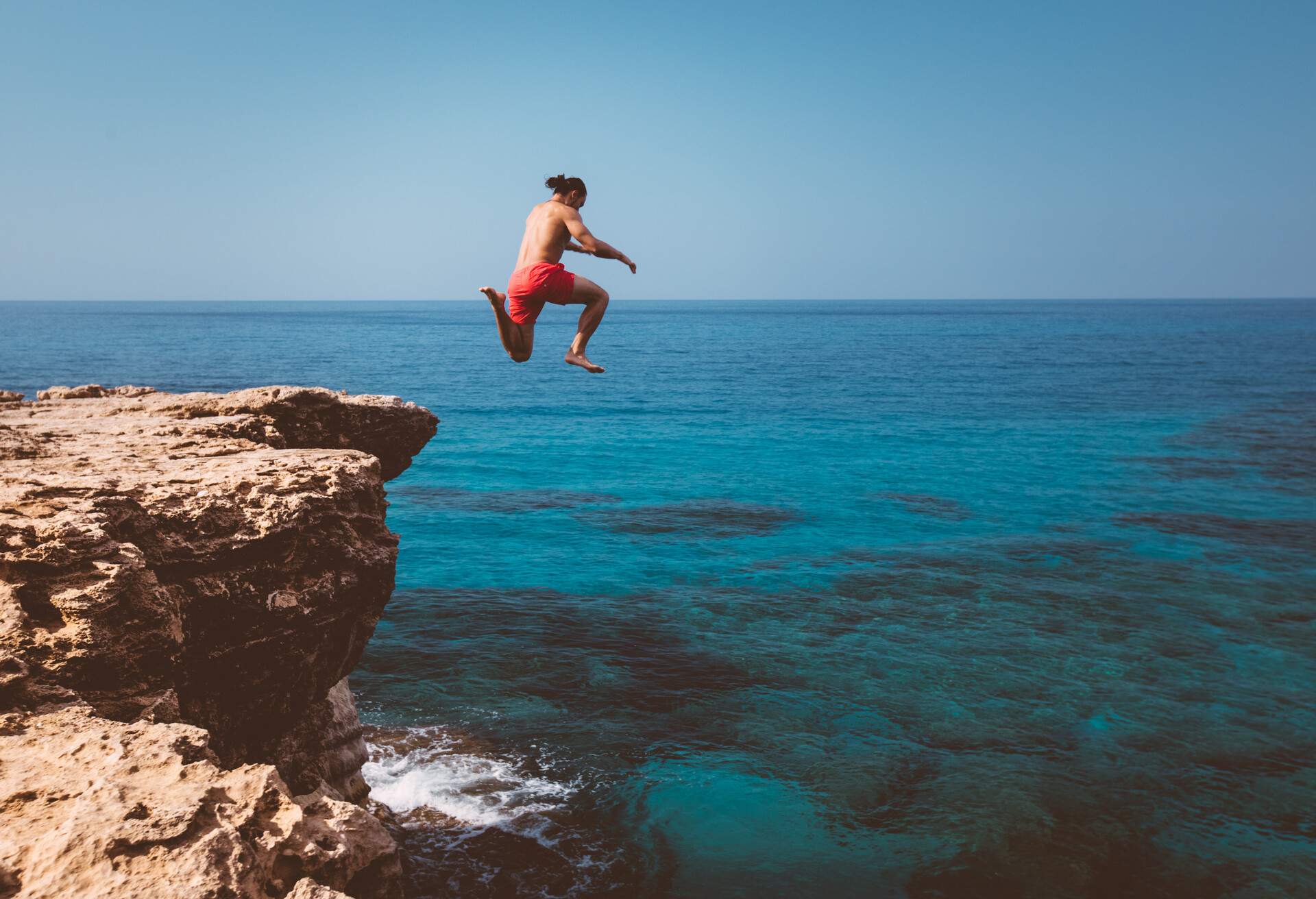 Brave man diving from high cliff into blue sea waters on tropical island summer adventure